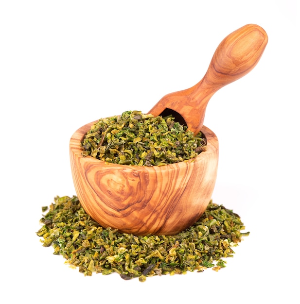 Dried green paprika flakes with seeds in olive bowl and scoop, isolated on white background. Chopped jalapeno, habanero or chilli pepper. Spices and herbs.