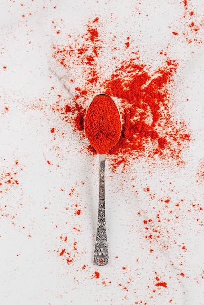 Dried ground chili pepper in spoon on white marble  top view copyspace