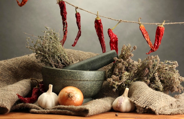 Dried herbs in mortar and vegetables on wooden table on grey background