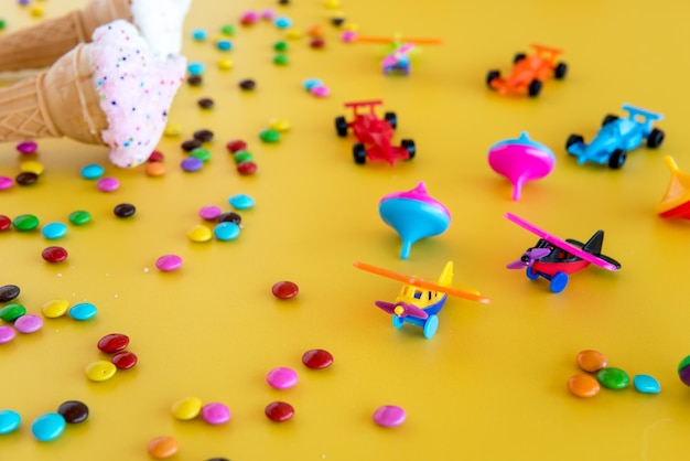 Dried ice cream colorful chocolates and plastic toys on a yellow background