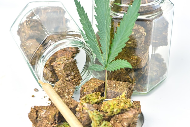 Dried marijuana in a jar with green marijuana leaves and rolls on a white background Medical marijuana dispensary Alternative medicine Cannabis plantation for medical and business concept