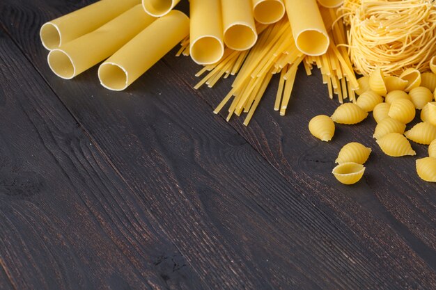 Dried mixed pasta on the dark wooden table, with copy space