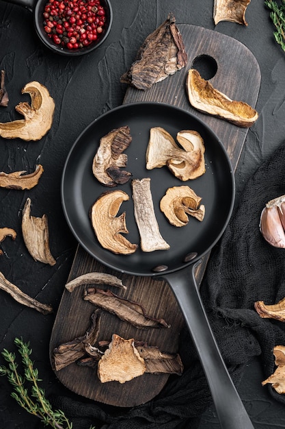 Dried mushrooms set in cast iron frying pan on black background top view flat lay