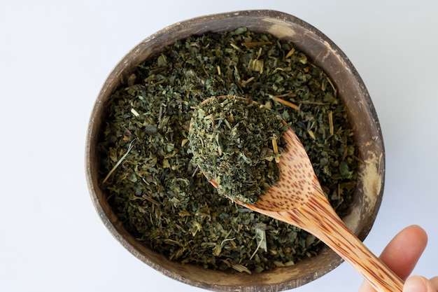 Dried nettle leaves for making medicinal tea in a wooden spoon on a beige background with a plate