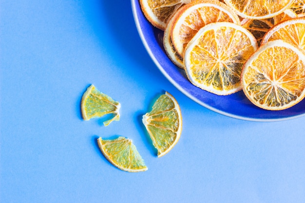 Photo dried orange fruit slices on a blue ceramic plate, blue paper fruit minimal concept.