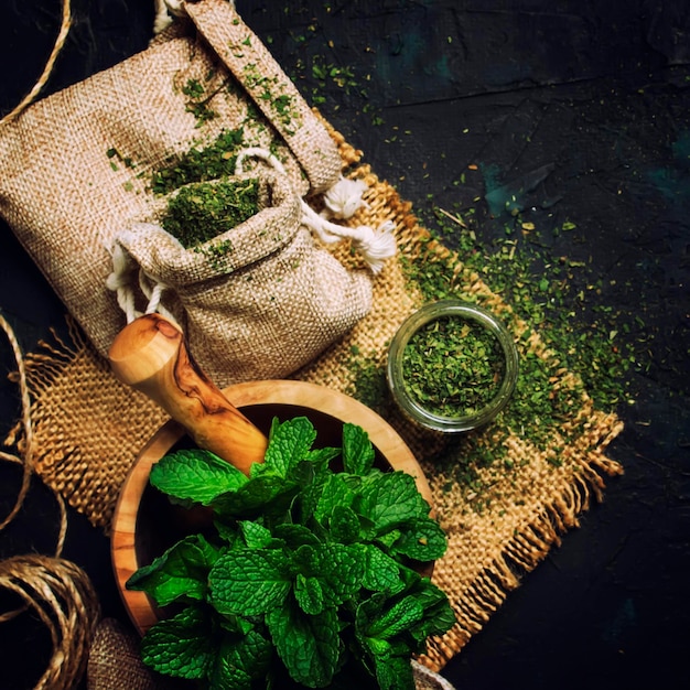 Dried peppermint in a glass jar and a bunch of fresh mint medicine herb on black background top view