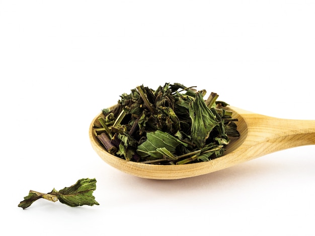 Dried peppermint leaves lie in a wooden spoon on a white 