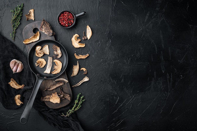 Dried porcini mushrooms set in cast iron frying pan, on black background, top view flat lay , with space for text copyspace