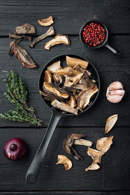 Photo dried porcini mushrooms set in cast iron frying pan, on black wooden table background, top view flat lay