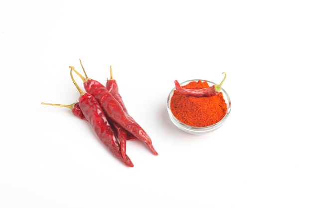 Dried red chilli and powder in glass bowl on white surface