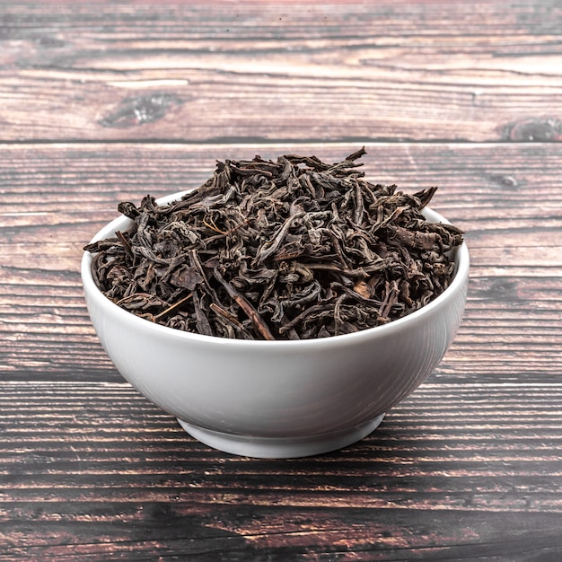 Dried tea is poured into a ceramic cup on a wooden plank table.