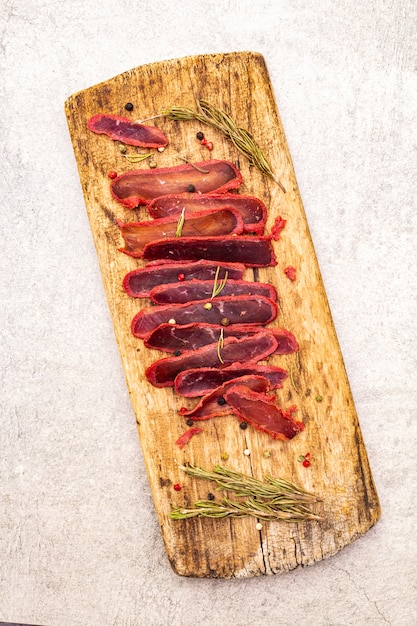 Dried tenderloin of beef meat with dry rosemary and pepper mix on vintage wooden board