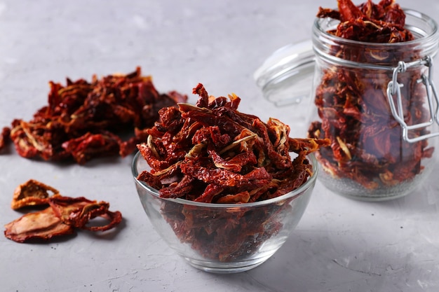 Dried tomatoes in bowl and glass jar on a gray concrete background. Horizontal format. Closeup