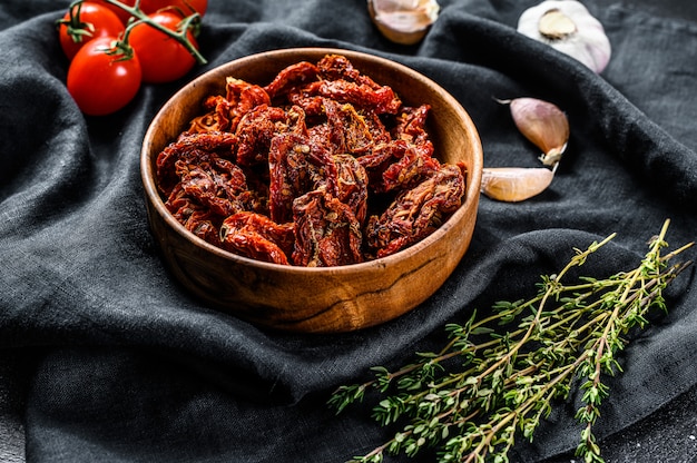 Dried tomatoes with garlic, spices and herbs. Recipe for cooking with ingredients. Black, dark surface. Top view