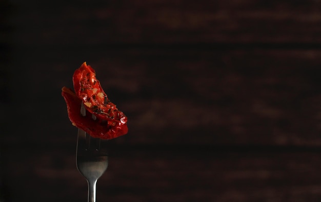 Dried tomatoes with Italian herbs on a fork on a dark background