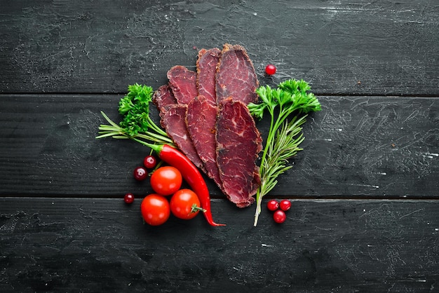 Dried veal beef with spices and herbs Beef jerky on old black table Top view Free space for your text