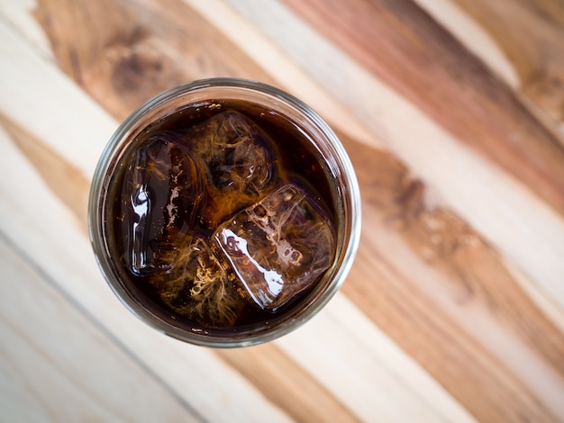 Drink cola with ice in glass on wooden table