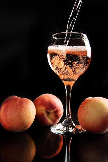 Drink crystal glass being served sparkling wine with peaches around and black background selective focus