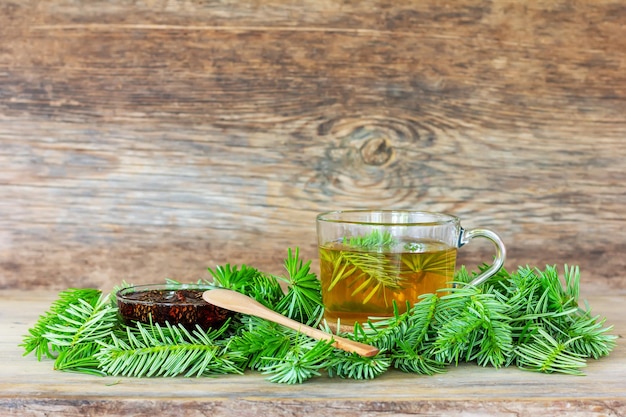 A drink made of pine needles in a cup with green fir needles and pine cone jam on a wooden background with a closeup copy space