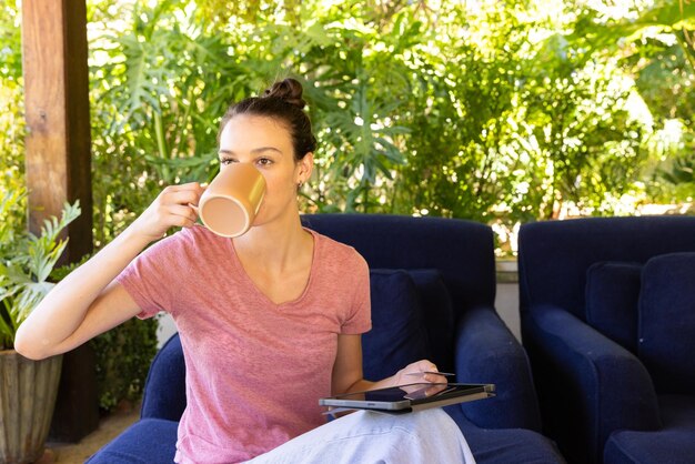 Photo drinking coffee woman using tablet while relaxing on blue couch