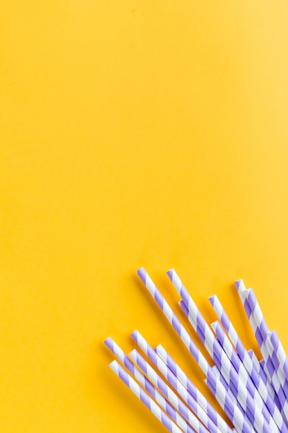 Drinking straws for party on yellow background. Top view of colorful paper, eco-friendly straws for summer cocktails. Drinking paper colorful straws for summer drinks.