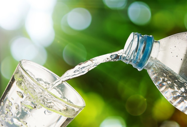 Drinking water is poured from a bottle into a glass on green bokeh background