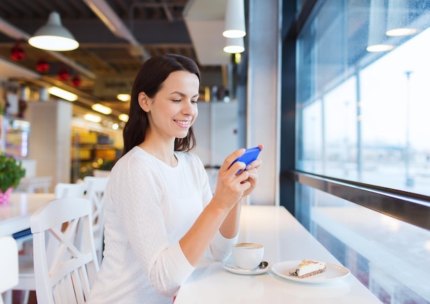 drinks, food, people, technology and lifestyle concept - smiling young woman with smartphone drinking coffee at cafe