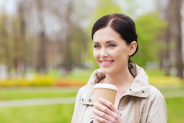 drinks, leisure and people concept - smiling woman drinking coffee in park