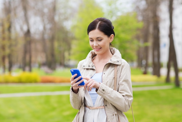 drinks, leisure, technology and people concept - smiling woman calling and talking on smartphone in park