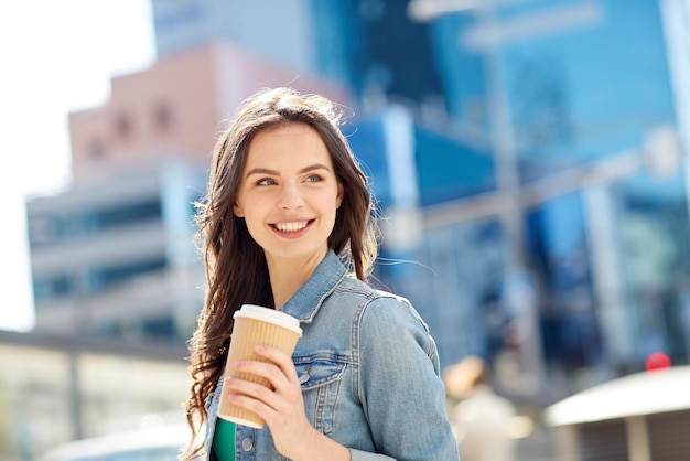 drinks and people concept - happy young woman or teenage girl drinking coffee from paper cup on city street