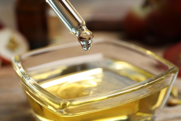 Dripping natural grape seed oil from pipette into bowl on wooden table closeup Organic cosmetic