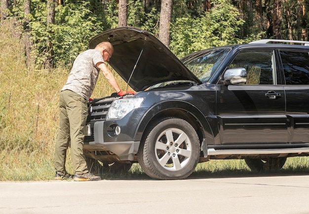 Driver standing and looking inside hood up with problem after car break in summer trip