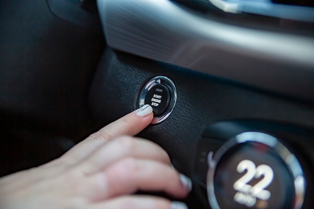 Photo drivers hand finger presses the start stop button in a modern car. close-up. no face. keyless option in car. selective focus