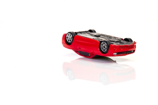 Driving car in alcoholic intoxication: red toy car lies upside down on white