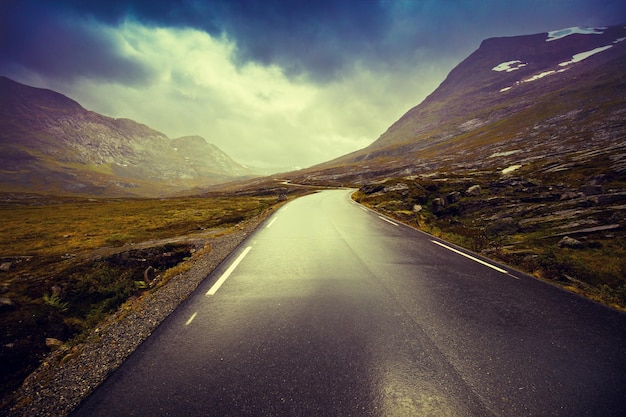 Driving a car on mountain road Road among mountains with dramatic stormy cloudy sky landscape Beautiful nature Norway Sunset