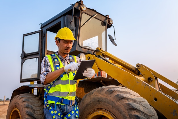 Driving worker heavy wheeled tractor, Workers drive orders through the tablet, Wheel loader Excavator with backhoe unloading sand works in construction site.