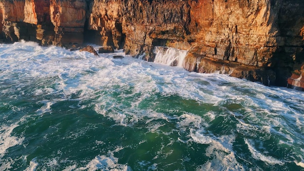 Drone powerful ocean waves breaking on high coastal rocks with bubbling foam