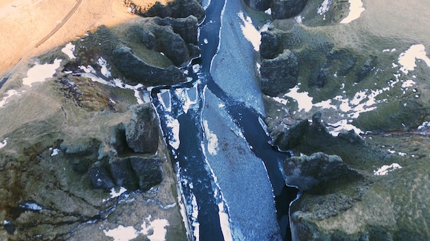 Drone shot of icelandic canyon with water stream and snowy mountains forming beautiful landscape. Majestic fjadrargljufur canyon with river in iceland, natural arctic scenery. Slow motion.