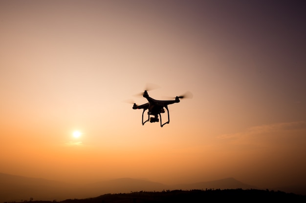 Drone silhouette flying in sunset landscape with digital camera at sunset ready to fly.