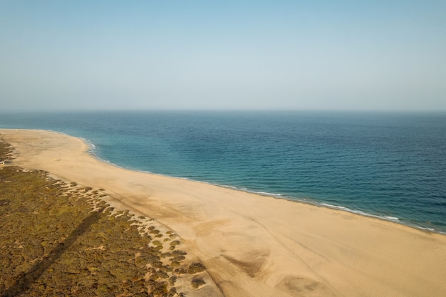 Drone view of long sandy shore near calm sea with blue water in summer evening