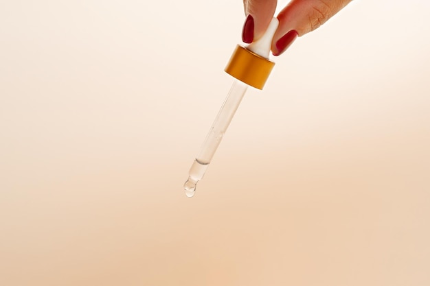 A drop on the end of the pipette of the red dropper bottle with face serum Product presentation