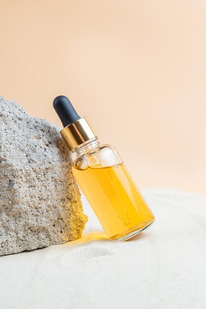 Dropper bottle of moisturizer serum or Vitamin C oil for face on stones with sand sand background summer face care