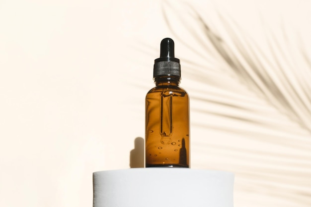 A dropper bottle of serum or liquid collagen on a beige background with a shadow from palm leave