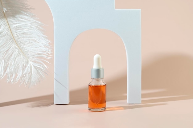 A dropper bottle with an orange nail cuticle oil standing in a white arche between geometric podiums