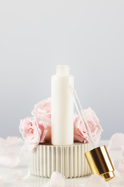 Dropper bottle with serum on a marble podium with tender pink roses