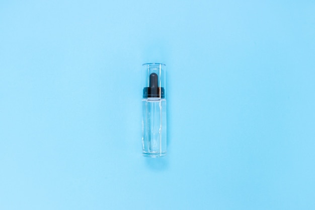 Dropper glass Bottle. Cosmetic pipette on blue. Flat lay