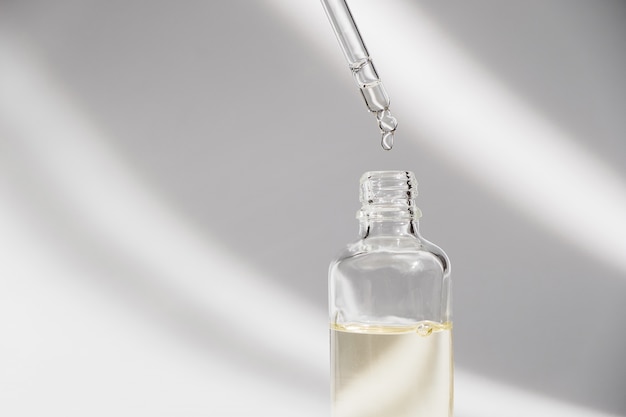 Dropper glass Bottle Mock-Up. Oily drop falls from cosmetic pipette on white background