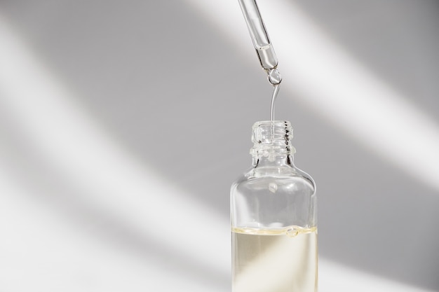 Dropper glass Bottle Mock-Up. Oily drop falls from cosmetic pipette on white background