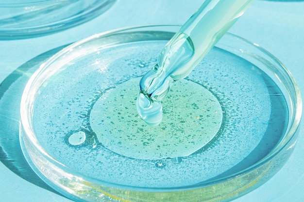 Dropping gel from a pipette into a Petri dish on a blue background Cosmetics Lab Serum gel retinol oil