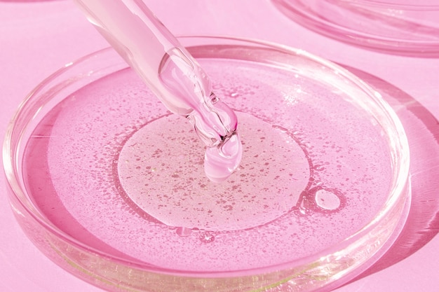 Dropping gel from a pipette into a Petri dish on a pink background Cosmetics Lab Serum gel retinol oil